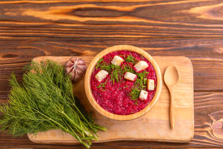 Bright tasty pureed beetroot soup in wooden bowl with ingredients on cutting board. Healthy food...