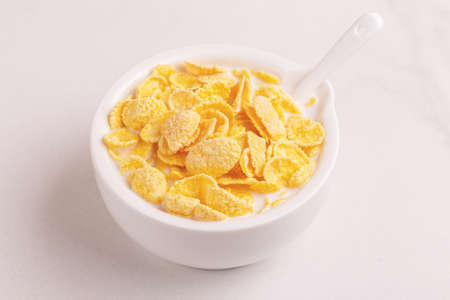 Fresh corn flakes in bowl with milk on light marble background. Healthy cereals breakfast. Copy...