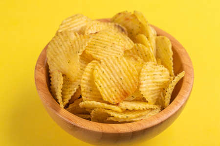 Crunchy corrugated potato chips in wooden bowl on bright yellow background. Junk food. Copy spaceの写真素材