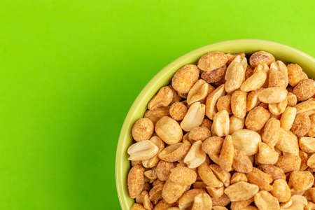 Roasted peanuts in bowl on bright green background. Movie snacks. Copy spaceの写真素材