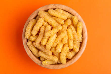 Crunchy corn sticks in wooden bowl on bright colored background. Snacks for watching movies. Copy...