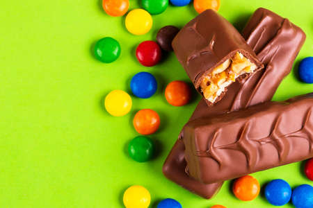 Tasty chocolate bars with nuts, toffee and colorful glazed round candies on bright green background....