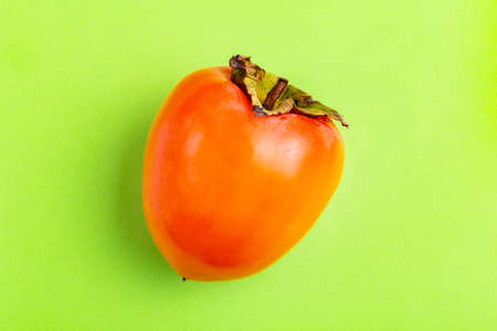 Delicious ripe persimmon fruit on bright green background. Seasonal winter fruit. Copy space