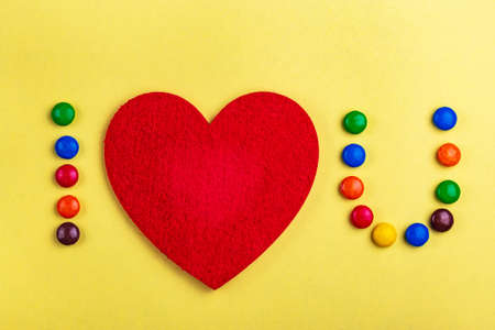 Love confession with help of glazed colorful chocolate candies and felt heart on yellow background. Valentine's day. Flat layの写真素材