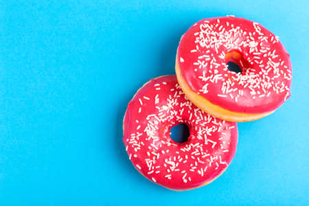Two delicious pink donuts with sprinkle on bright blue background. Unhealthy, but tasty sweets. Copy...