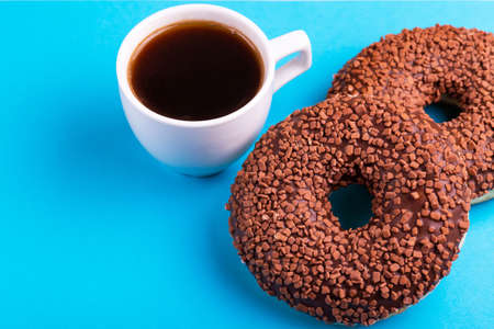Two tasty chocolate donuts with cup of strong coffee on bright blue background. Unhealthy, but delicious sweets. Copy space. Top viewの写真素材