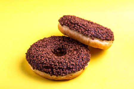 Two delicious chocolate donuts with sprinkle on bright yellow background. Unhealthy, but tasty...