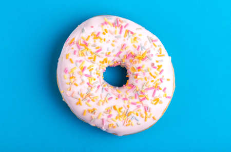 Tasty vanilla donut with sprinkle on bright blue background. Unhealthy, but delicious sweets. Copy space. Top viewの写真素材
