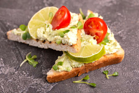 Toasts with avocado pate, fresh microgreen and cherry tomatoes on dark concrete background. Healthy...