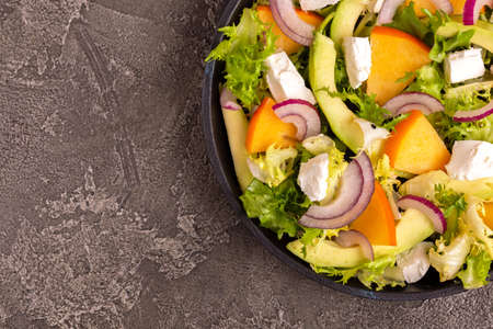 Delicious salad with frisee, persimmon, feta, chicken fillet and onion in cast-iron pan. Dark...