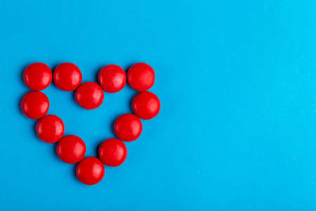 Little glazed chocolate red candies shaped into heart on bright blue background. Valentine's day....