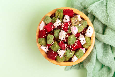Unusual salad with raw beetfoot, feta cheese and sesame in wooden bowl on light green background....
