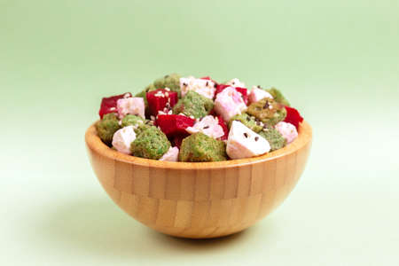 Unusual salad with raw beetfoot, feta cheese and sesame in wooden bowl on light green background....