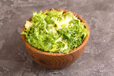 Fresh frisee salad in wooden bowl. Healthy food. Dark concrete background. Copy spaceの写真素材