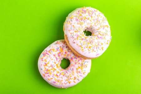 Two delicious vanilla donuts with sprinkle on bright green background. Unhealthy, but tasty sweets. Copy space. Top viewの写真素材