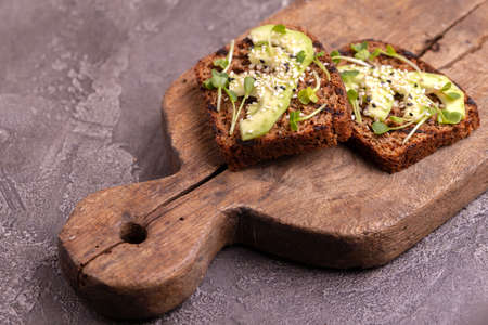 Healthy rye toasts with avocado, radish sprouts and sesame on burlap napkin. Wooden background....