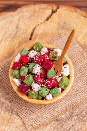 Unusual salad with raw beetroot, feta cheese and sesame in wooden bowl on burlap napkin. Rustic wooden background. Copy spaceの写真素材