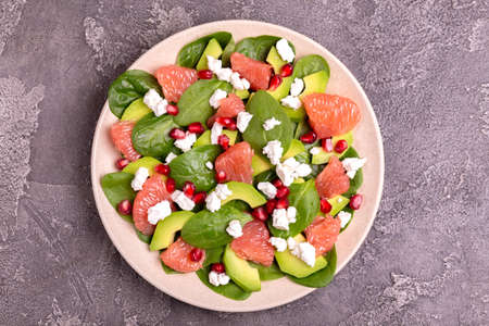 Tasty salad with grapefruit, spinach, feta, avocado and pomegranate is served in plate. Healthy food concept. Dark concrete background. Copy spaceの写真素材