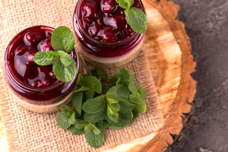 Layered cherry bisquit dessert with ricotta, mint and honey in glass jar. Yogurt cheesecake...