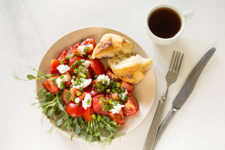 Healthy breakfast salad with tomatoes, avocado, bun, pea sprouts, ricotta, pesto and coffee. White...