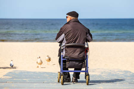 Disabled older man sitting in a wheelchair and looks at the seaのeditorial素材