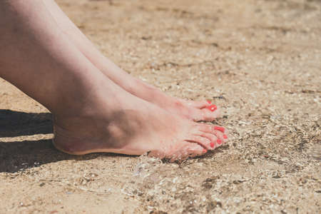 female feet with red pedicure in beach sand, close upの写真素材