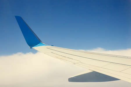 Wing of an airplane flying above the clouds on blue sky backgroundの写真素材