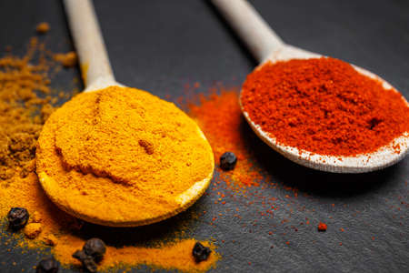 spices in wooden spoons over black stone background, top viewの写真素材