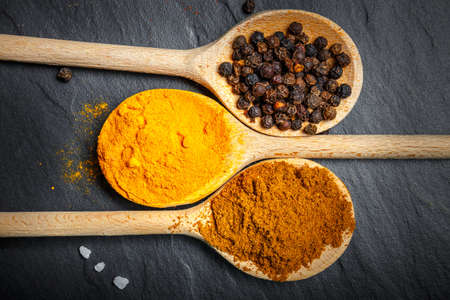 spices in wooden spoons over black stone background, top viewの写真素材