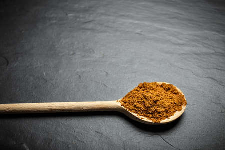 spices in wooden spoons over black stone background, top view