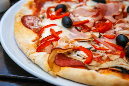 Pizza with red fresh paprika and black olives on white plateの写真素材
