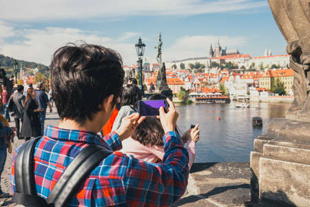 Prague, Czech Republic, September 30, 2017: Young man is taking photos with his smartphone on Charles Bridge during beautiful autumn day, Prague, Czech Republicのeditorial素材