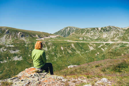 Woman sits on the top and admires the beautiful view of Parang mountains, Romaniaの写真素材