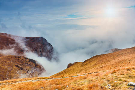 mountain landscape with fog below the peaks and clouds above them in blue tones