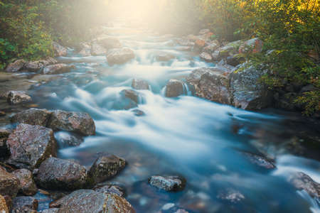 Beautiful waterfall in the mountains with the rays of the sun shining through the treesの写真素材