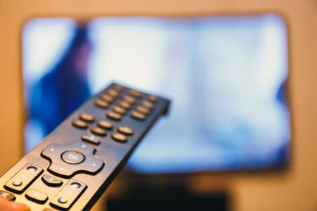 Hand holding TV remote control and presses the buttonの写真素材