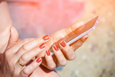 female hands with red manicure holding cell phoneの写真素材