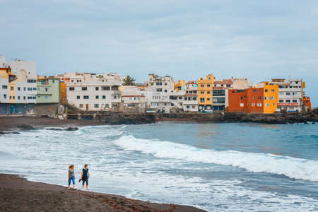 Puerto de la Cruz, Tenerife, Spain - June 08, 2015: Unknown people are walking and relaxing on the beach with colour houses in the background, Puerto de la Cruz, Tenerife Island, Spainのeditorial素材