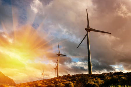 Windmills for electric power production in mountain during sunset