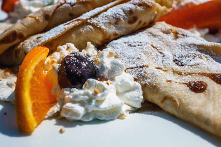 pancake with apple filling decorated with whipped cream, strawberries and orangesの写真素材