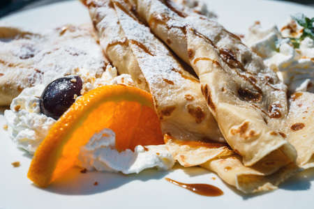 pancake with apple filling decorated with whipped cream, oranges and cherry