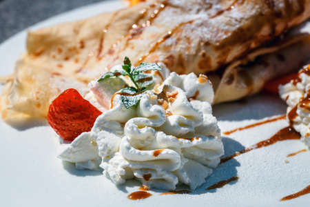 pancake with apple filling decorated with whipped cream, strawberries and orangesの写真素材