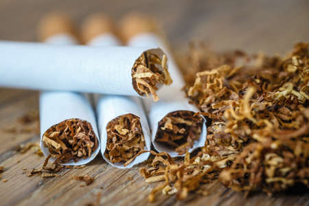 cut tobacco leaves and handmade cigarettes on a wooden background