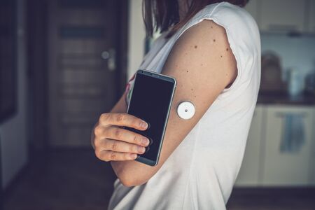 Woman checking glucose level with a remote sensor and mobile phone, sensor checkup glucose levels without blood. Diabetes treatment.の写真素材