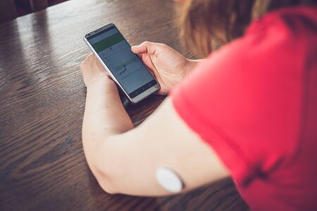 Woman checking glucose level with a remote sensor and mobile phone, sensor checkup glucose levels without blood. Diabetes treatment. Focus on background.の写真素材