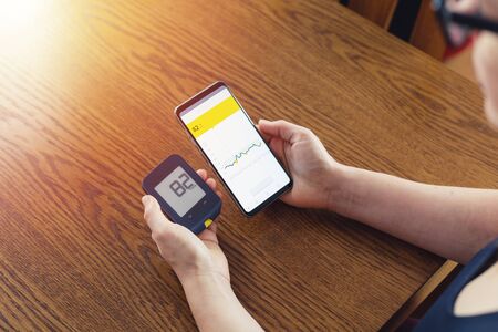 Woman comparing result of glucose level check on the traditional glucometer and on the mobile phone read from modern technology remote sensorの写真素材