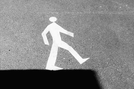Road sign on the asphalt - walking man on the edge of shadow.の写真素材