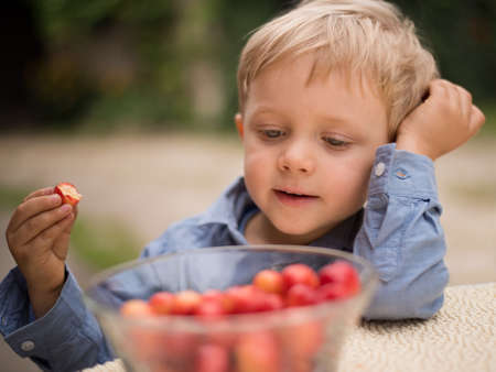 Closeup portrait of a little smiling boy eating cherryの写真素材