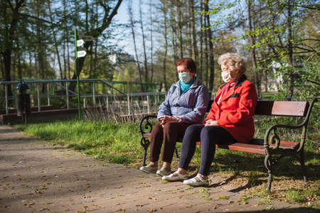 LUBIN, POLAND - APRIL 21, 2020. Two old women with obligatory face masks sits on the bench in the park during a pandemic Coronavirus Covid-19.のeditorial素材