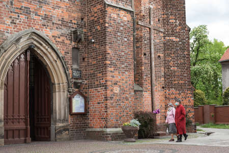 SCINAWA POLAND - MAY 3, 2020. People going to the Church of the Exaltation Holy Cross. Due to the pandemic Covid-19 coronavirus people have face masks and there is social distance.のeditorial素材
